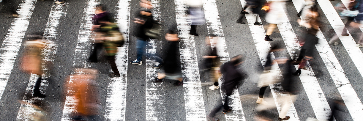 View from above of a crowd of pedestrians on a zebra crossing with motion blur to the walking people and focus to the stripes on the asphalt